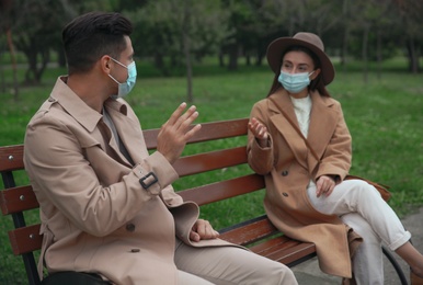Photo of Man and woman talking on bench in park. Keeping social distance during coronavirus pandemic