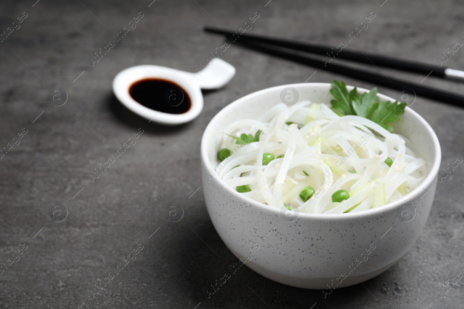 Photo of Bowl of rice noodles with chopsticks on grey background. Space for text