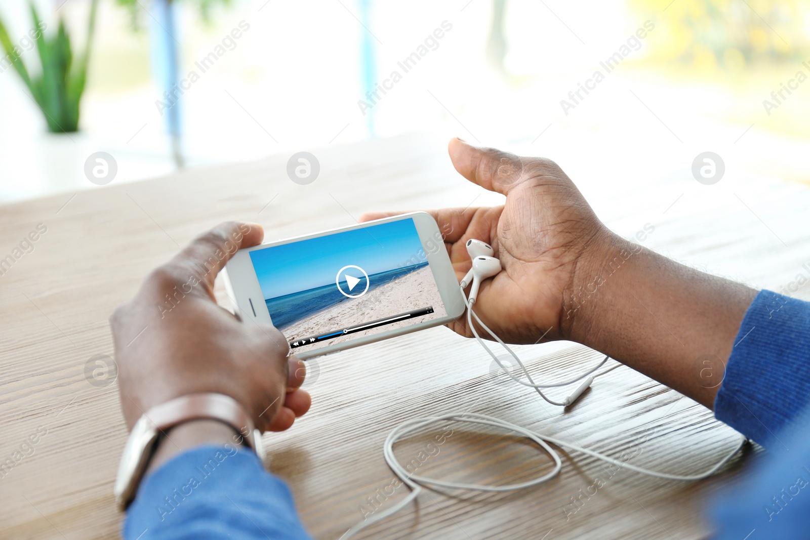 Image of Man watching video on mobile phone at wooden table, closeup