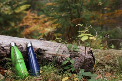 Two thermo bottles near log in autumn forest