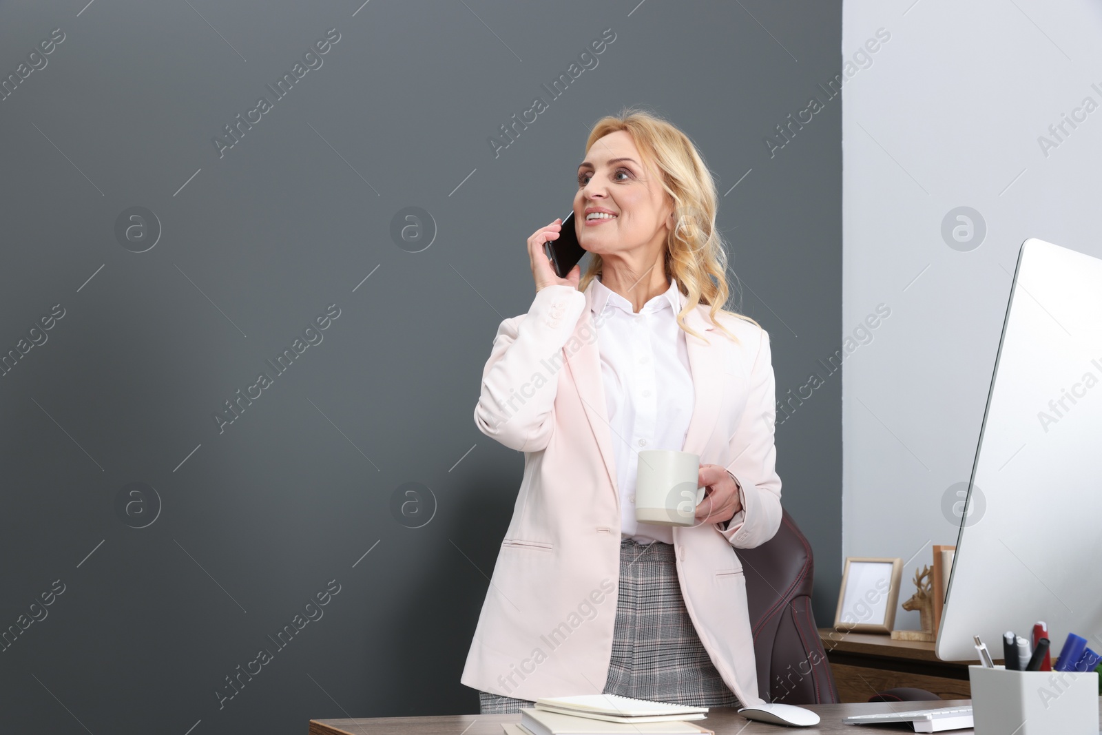 Photo of Lady boss talking on smartphone near computer in office, space for text. Successful businesswoman