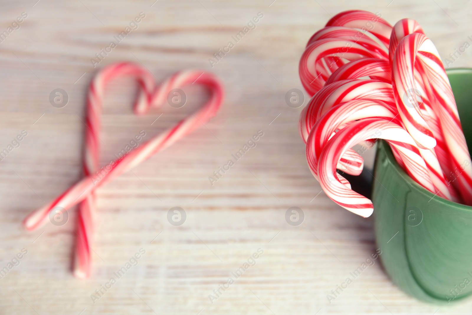 Photo of Tasty candy canes in cup on wooden table. Space for text