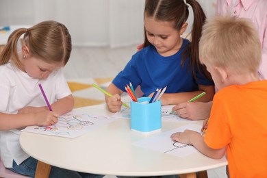 Photo of Nursery teacher and cute little children drawing pictures at desk in kindergarten. Playtime activities