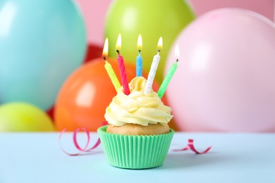 Photo of Birthday cupcake with burning candles and streamer on light blue table against color balloons