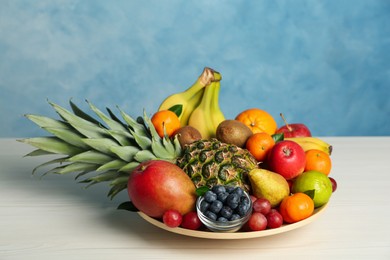 Photo of Assortment of fresh exotic fruits on white wooden table against light blue background