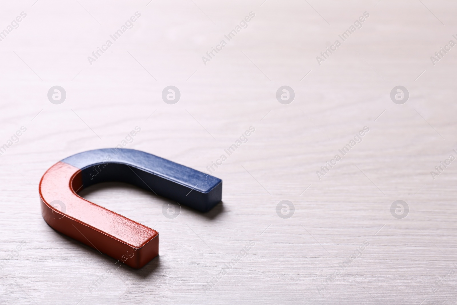 Photo of Red and blue horseshoe magnet on light wooden background. Space for text