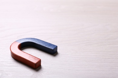 Red and blue horseshoe magnet on light wooden background. Space for text