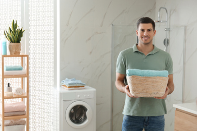 Happy man with laundry basket in bathroom