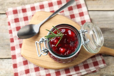 Photo of Fresh cranberry sauce in glass jar, rosemary and spoon on light wooden table, top view