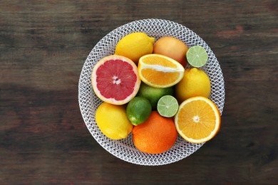 Photo of Bowl with different citrus fruits on wooden table, top view