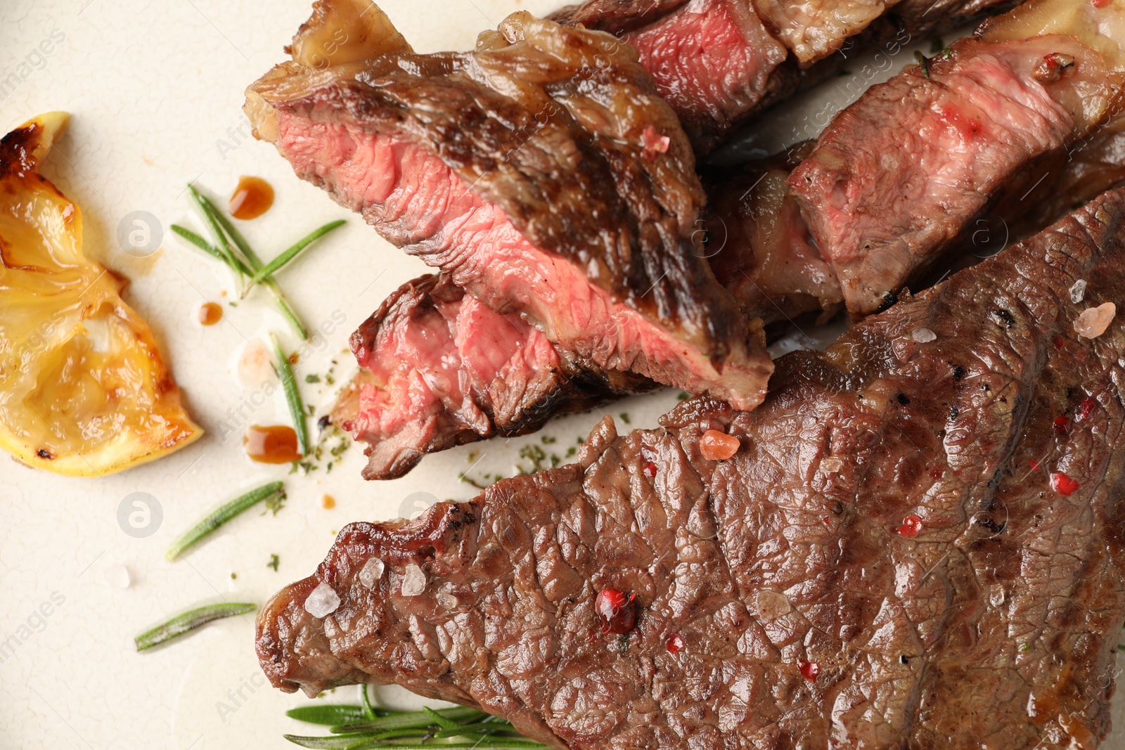 Photo of Delicious grilled beef steak, lemon slice and rosemary on plate, top view