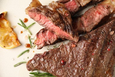 Photo of Delicious grilled beef steak, lemon slice and rosemary on plate, top view