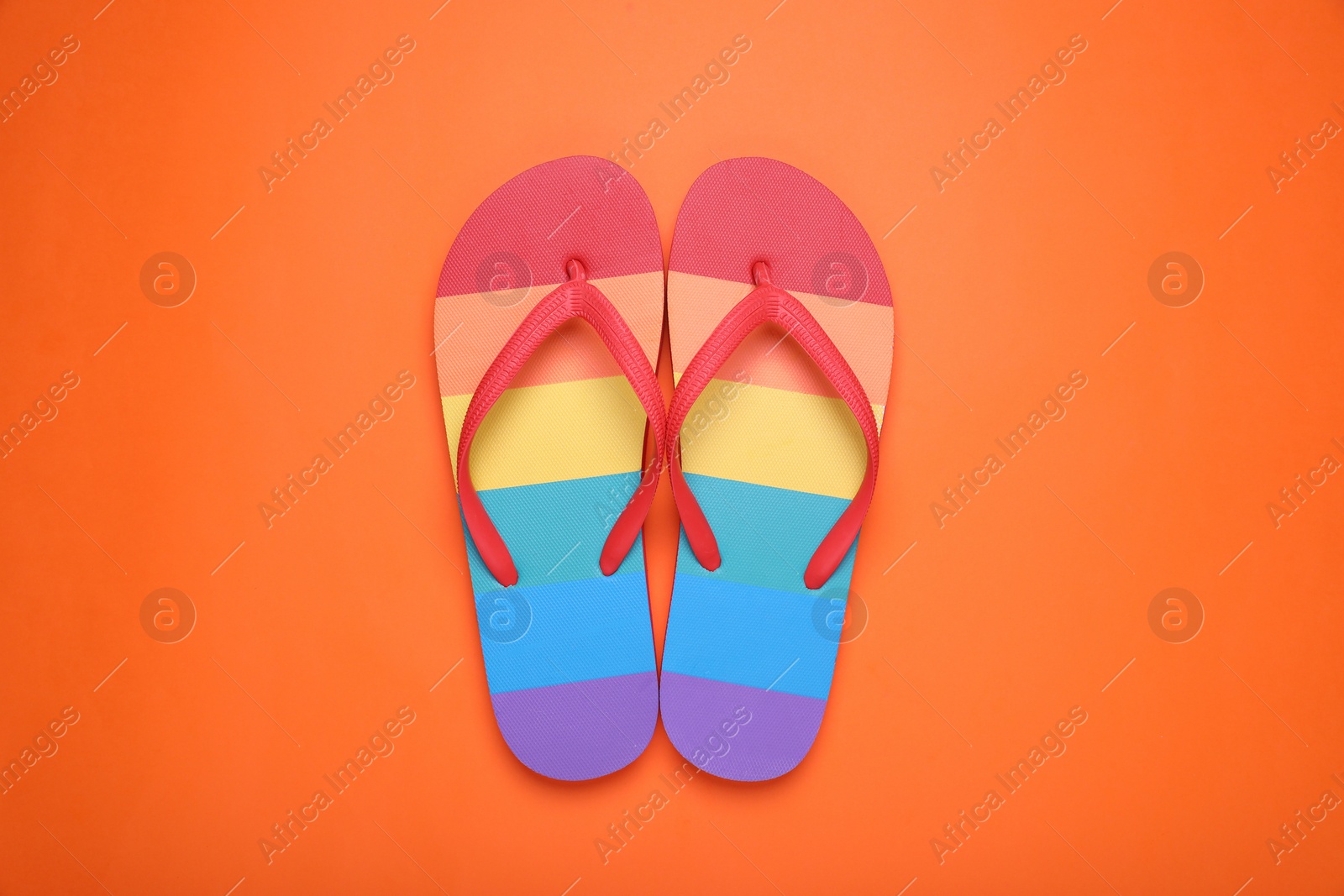 Photo of Rainbow flip flops on orange background, flat lay. LGBT pride
