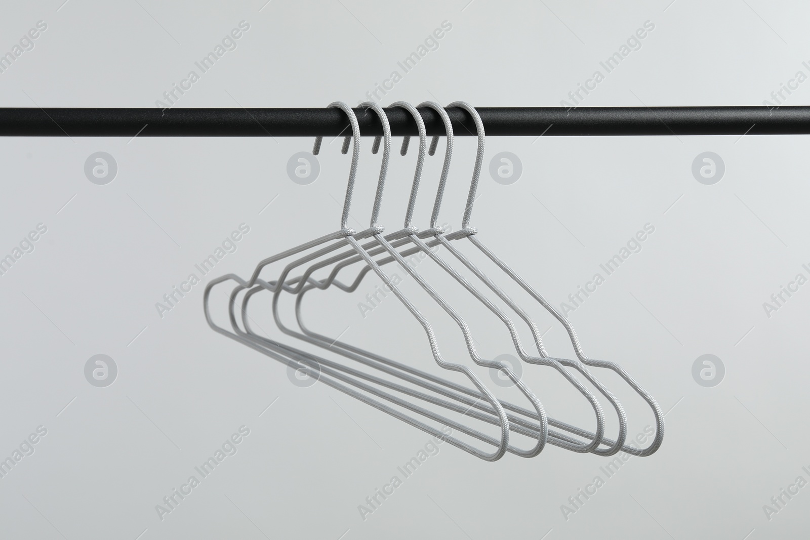 Photo of Empty clothes hangers on black rack against light grey background