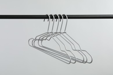 Photo of Empty clothes hangers on black rack against light grey background