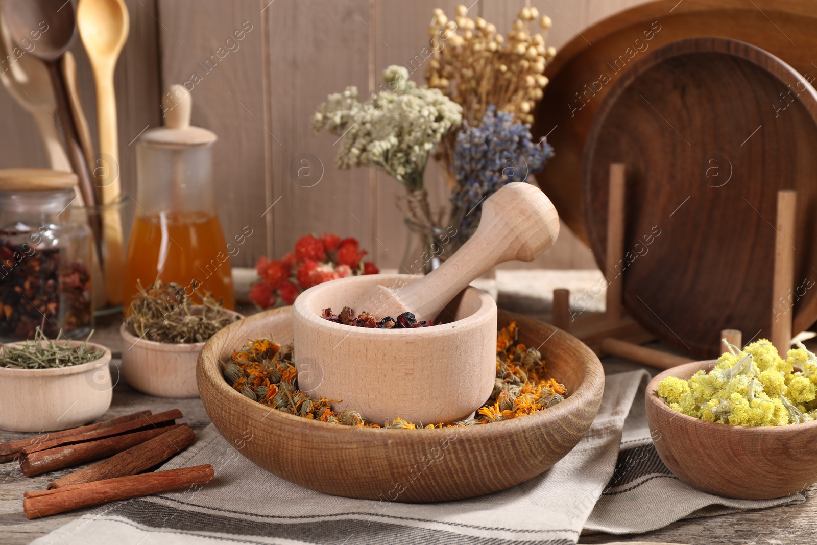 Photo of Mortar with pestle, many different dry herbs, flowers and cinnamon sticks on wooden table