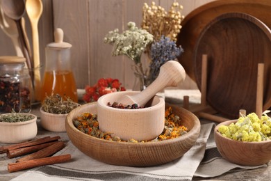 Mortar with pestle, many different dry herbs, flowers and cinnamon sticks on wooden table