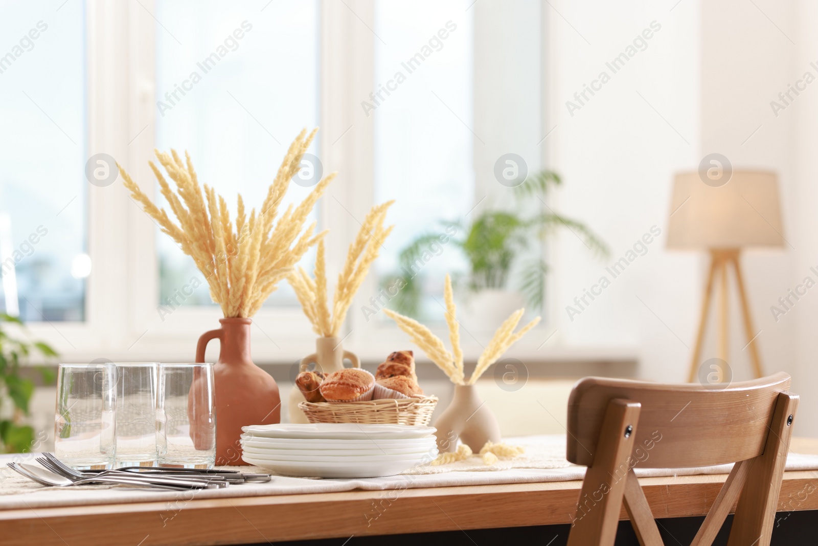 Photo of Clean dishes, dry spikes and fresh pastries on table in stylish dining room