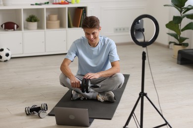 Smiling sports blogger holding ab roller while streaming online fitness lesson with smartphone at home