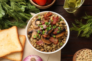 Photo of Delicious lentils with mushrooms, bacon and green onion in bowl served on wooden table, flat lay
