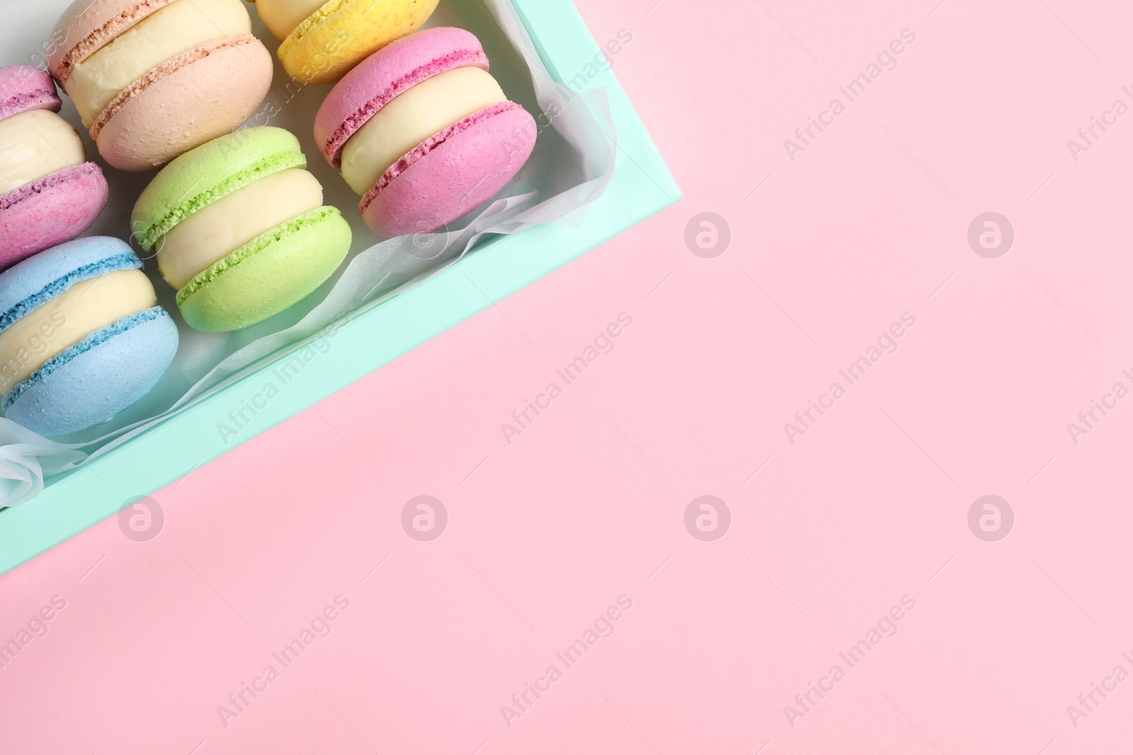 Photo of Many delicious colorful macarons in box on pink background, top view. Space for text