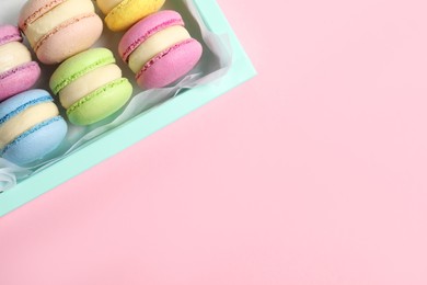 Photo of Many delicious colorful macarons in box on pink background, top view. Space for text