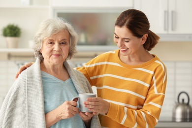Female caregiver and elderly woman with cup of tea in kitchen