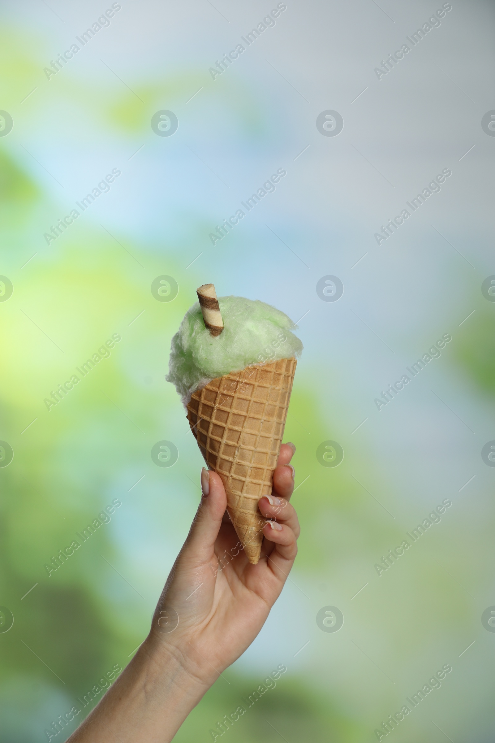 Photo of Woman holding waffle cone with cotton candy on blurred background, closeup