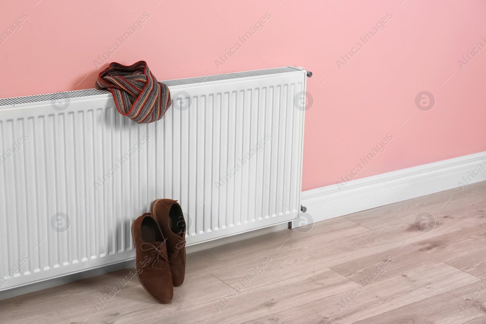 Photo of Heating radiator with scarf and shoes near color wall, Space for text