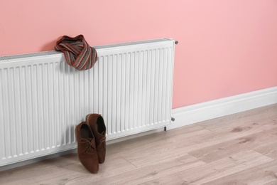 Photo of Heating radiator with scarf and shoes near color wall, Space for text