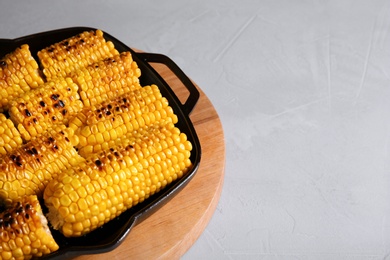 Photo of Fresh grilled tasty corn cobs in pan and space for text on light background