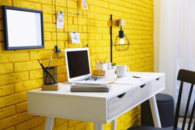 Photo of Stylish home office interior with comfortable workplace near yellow brick wall