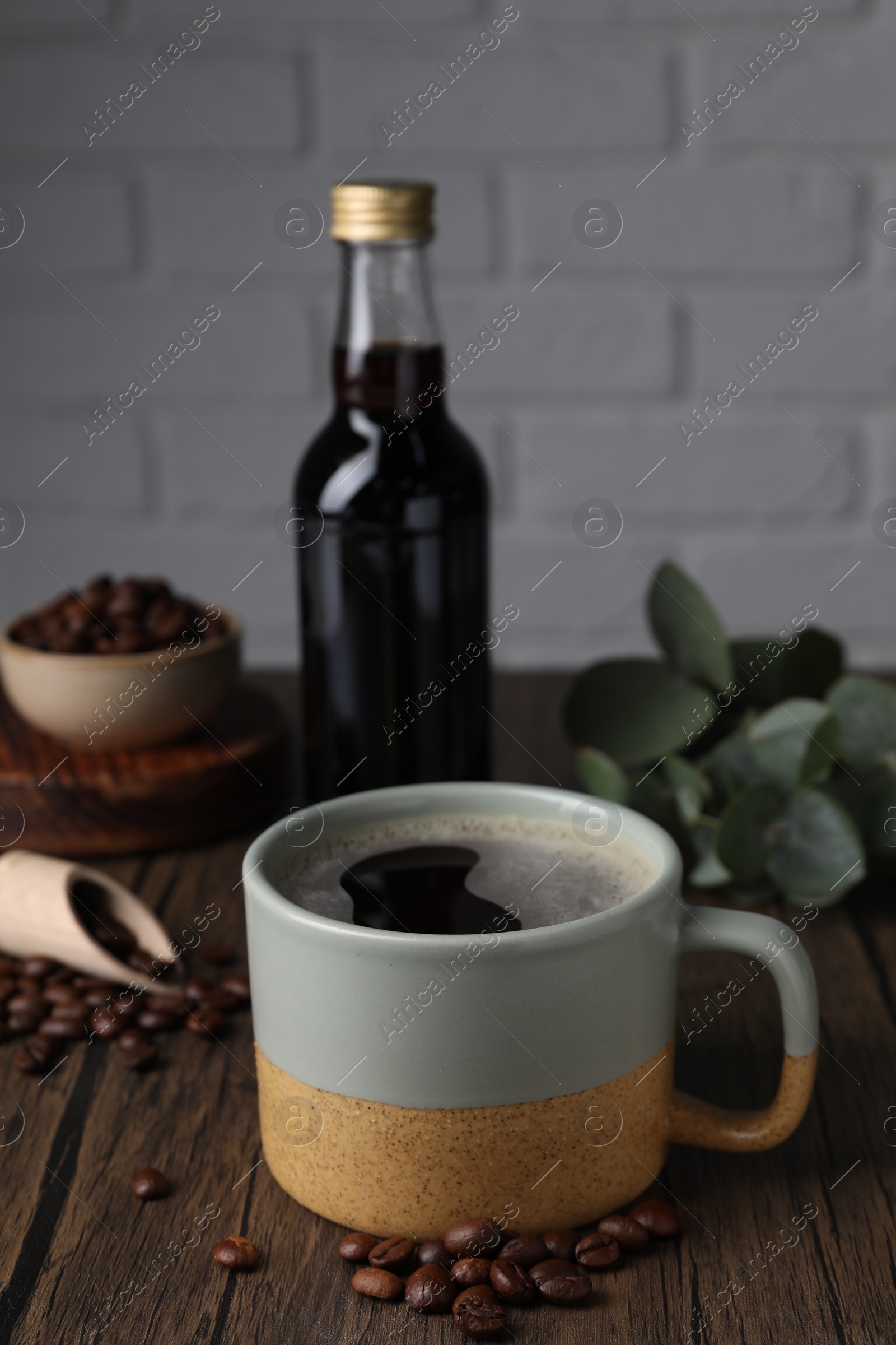Photo of Mug of aromatic coffee, syrup and beans on wooden table