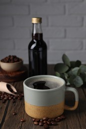 Mug of aromatic coffee, syrup and beans on wooden table