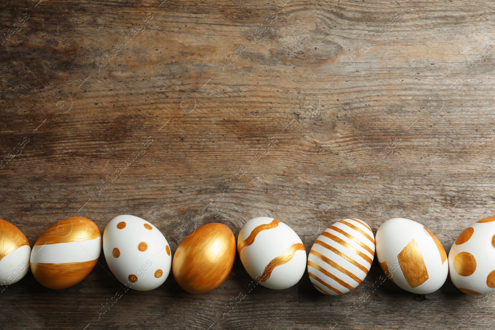 Photo of Set of traditional Easter eggs decorated with golden paint on wooden background, top view. Space for text