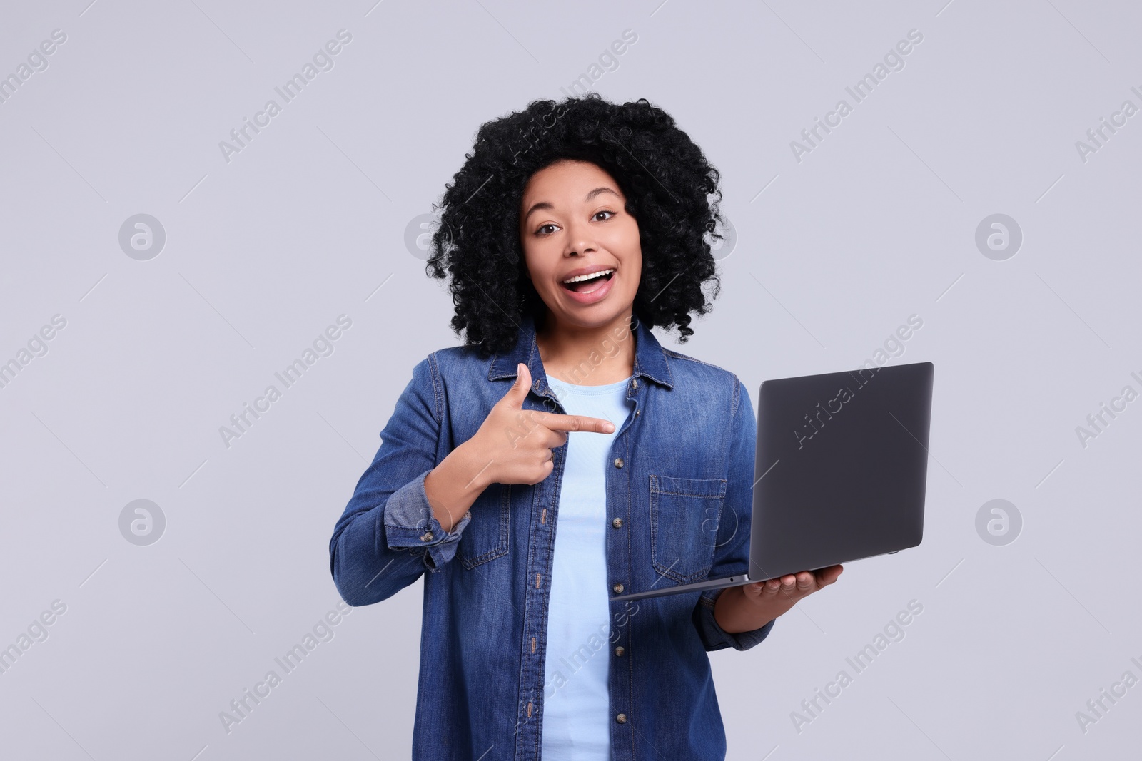 Photo of Happy young woman showing laptop on light grey background