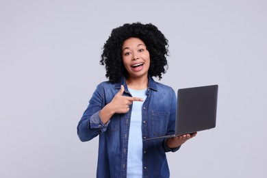 Photo of Happy young woman showing laptop on light grey background