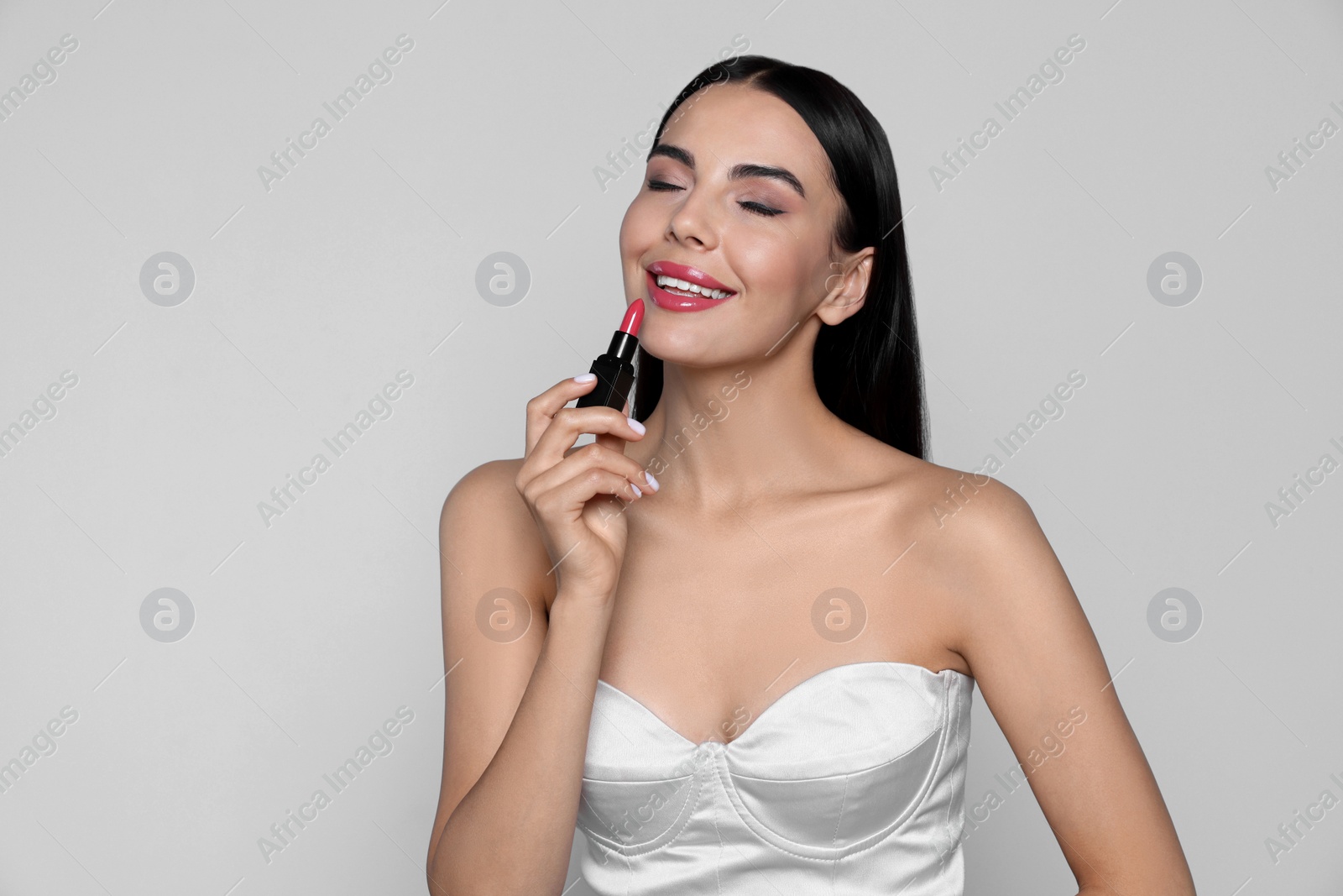 Photo of Young woman with beautiful makeup holding glossy lipstick on light gray background