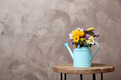 Photo of Watering can with beautiful wild flowers on table against grey background