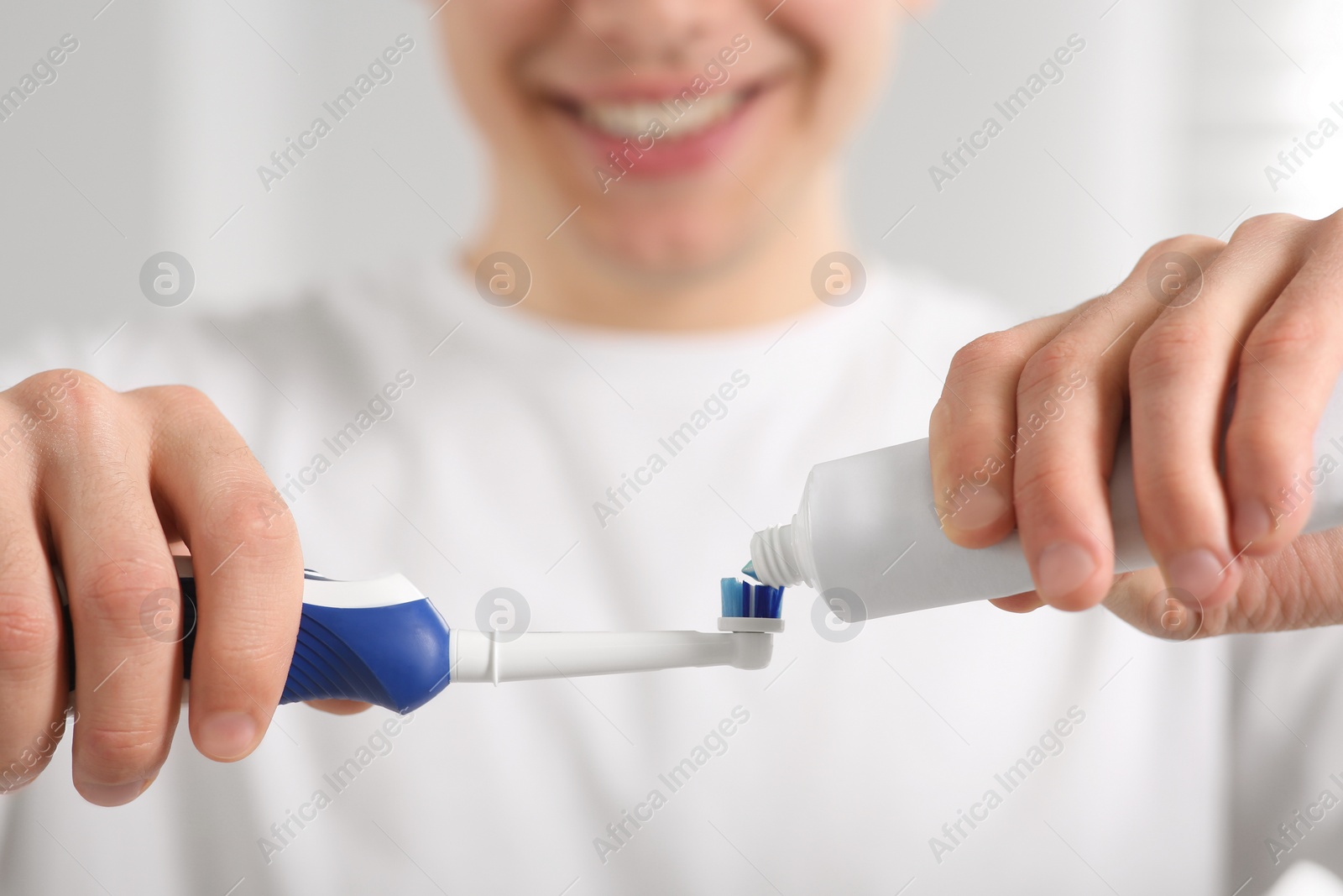 Photo of Man squeezing toothpaste from tube onto electric toothbrush on blurred background, closeup