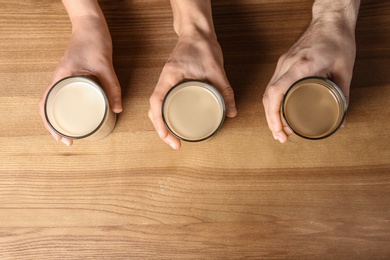 Photo of People holding glasses with protein shakes on wooden background, top view. Space for text