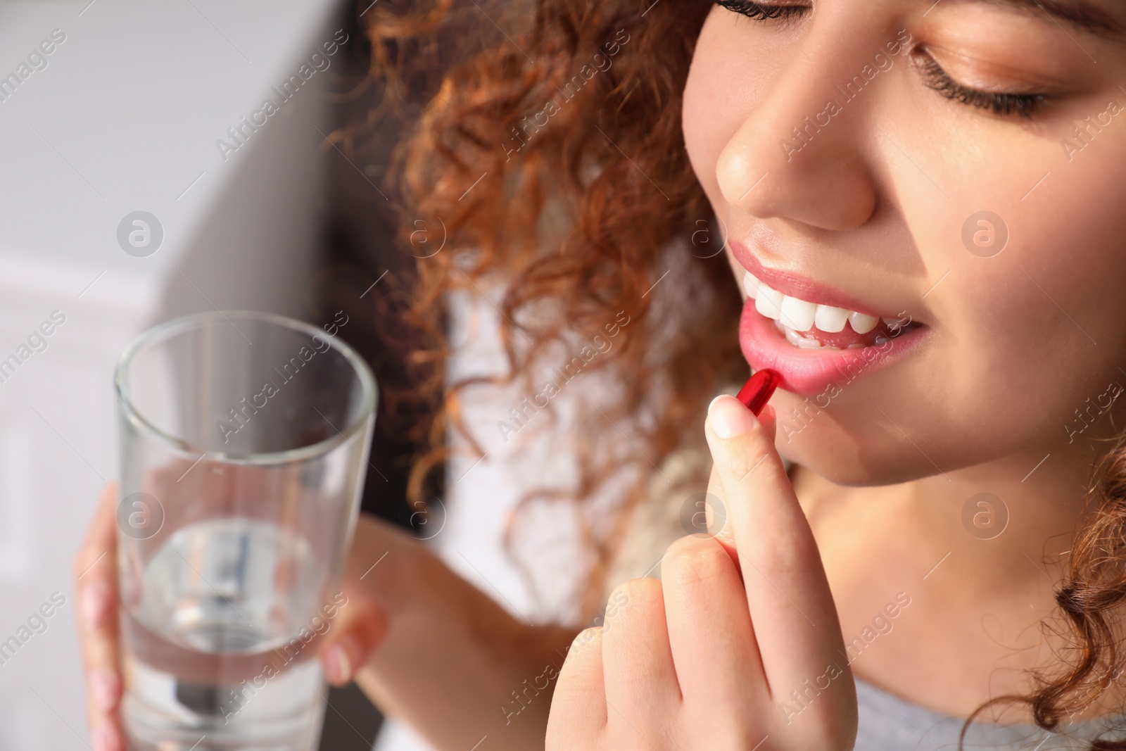 Photo of African-American woman with glass of water taking vitamin pill at home, closeup