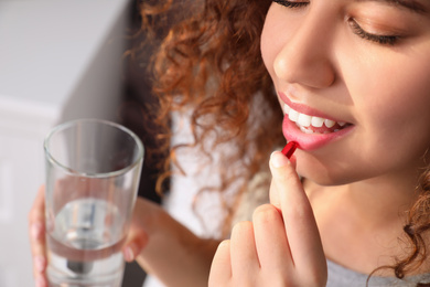Photo of African-American woman with glass of water taking vitamin pill at home, closeup