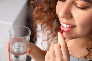 African-American woman with glass of water taking vitamin pill at home, closeup