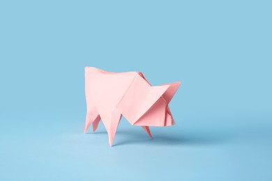 Photo of Origami art. Handmade pink paper pig on light blue background