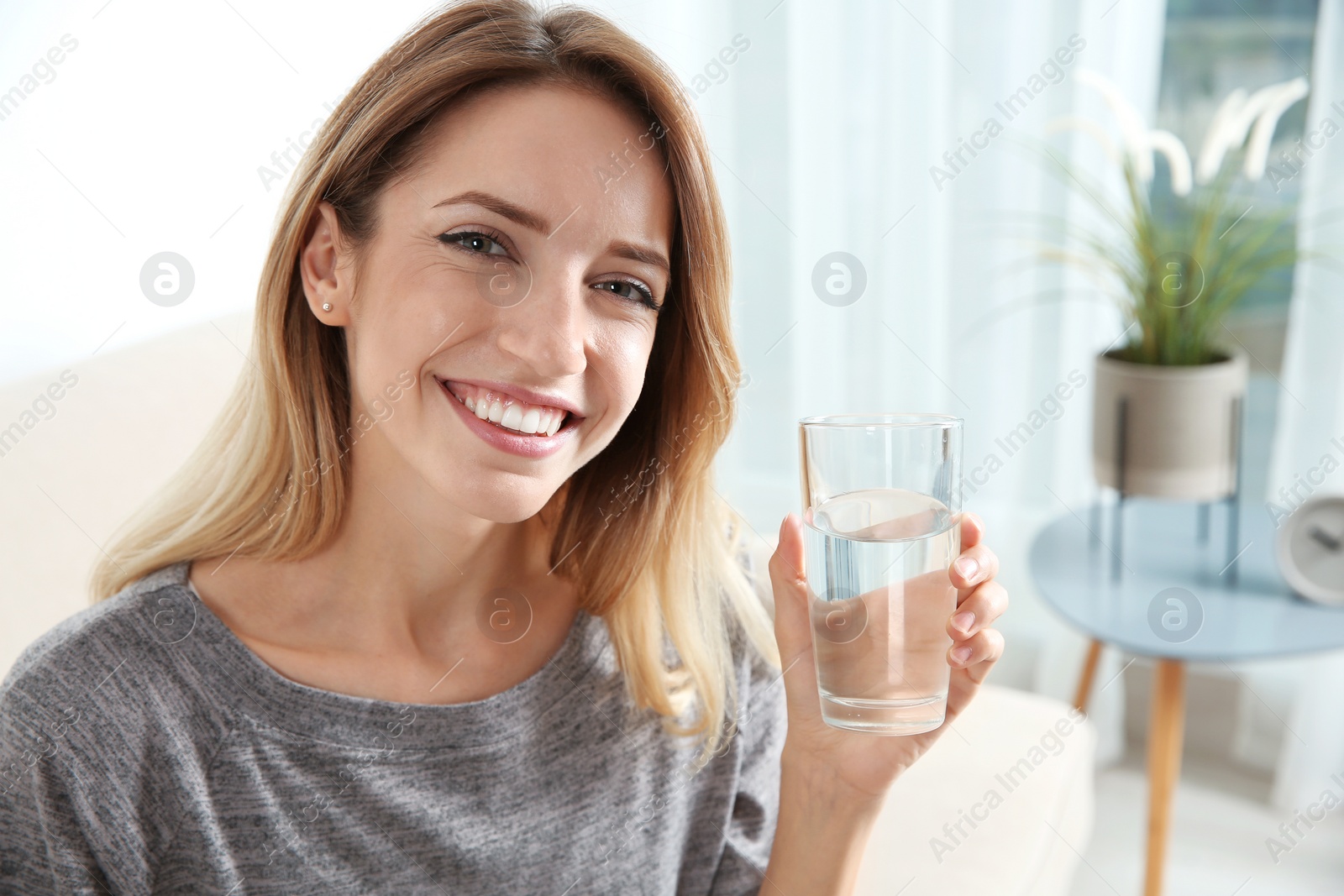 Photo of Young woman holding glass with clean water at home