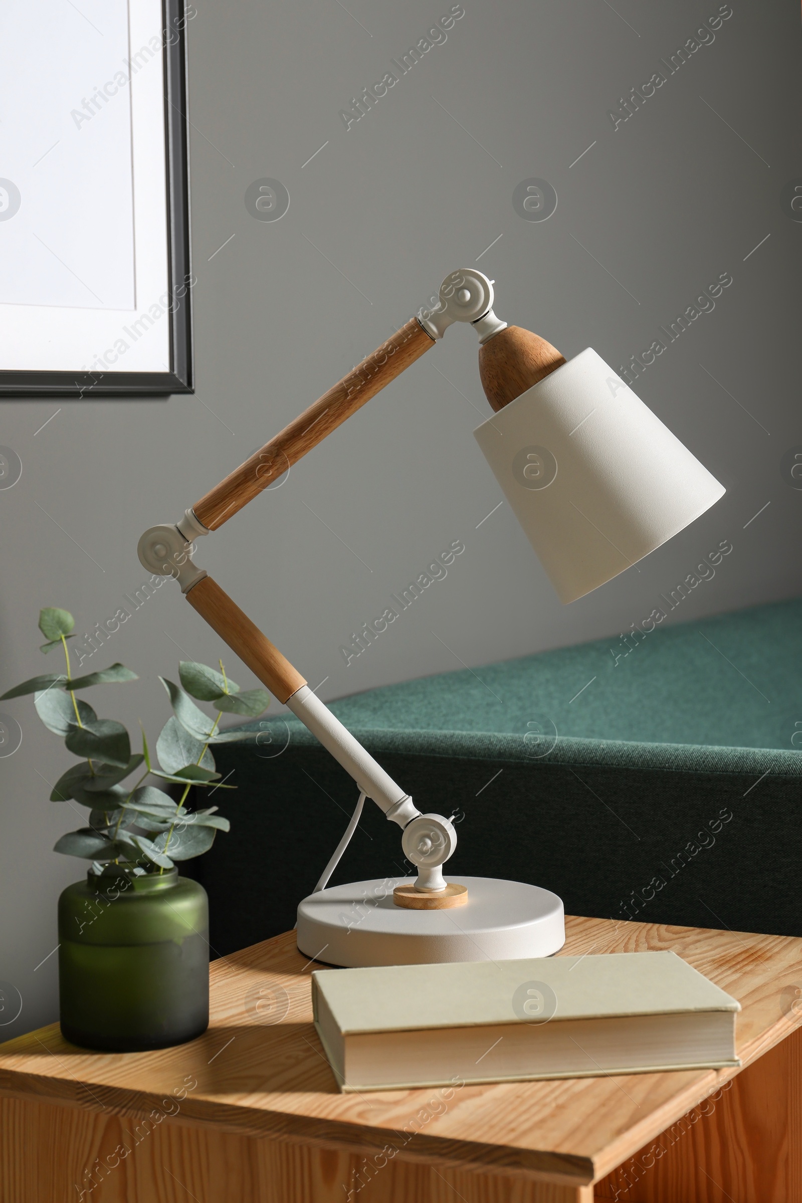 Photo of Stylish modern desk lamp, book and plant on wooden cabinet in living room