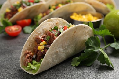 Delicious taco with meat and vegetables on gray textured table, closeup