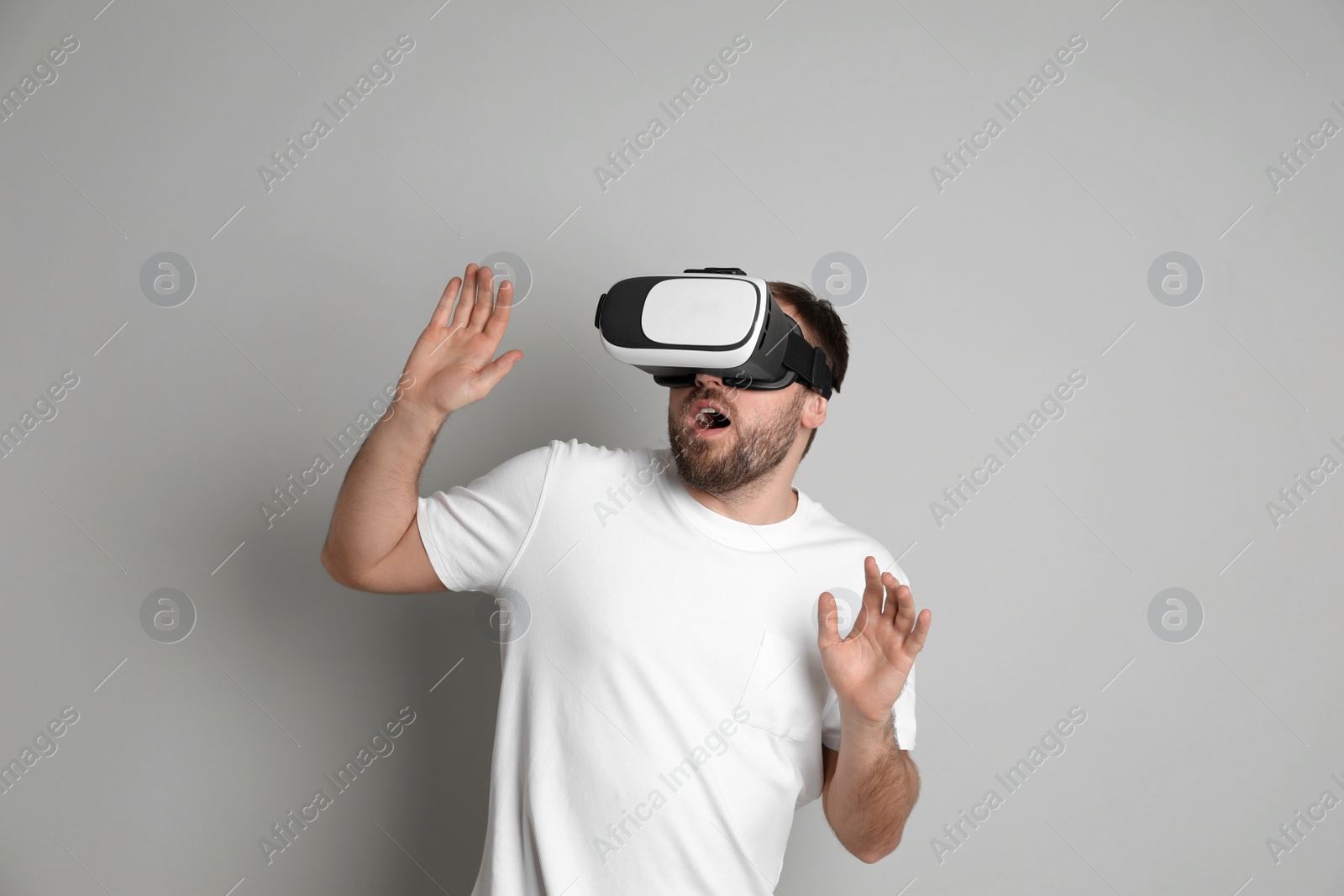 Photo of Emotional man using virtual reality headset on light grey background