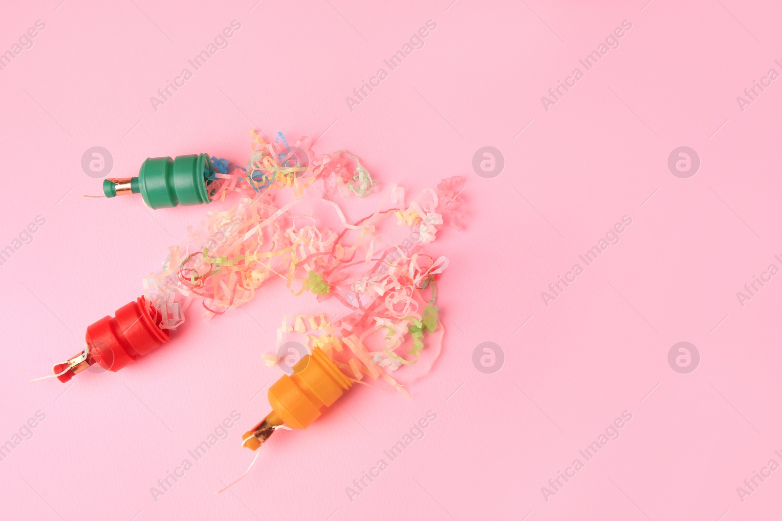 Photo of Beautiful serpentine bursting out of small party poppers on pink background, flat lay. Space for text